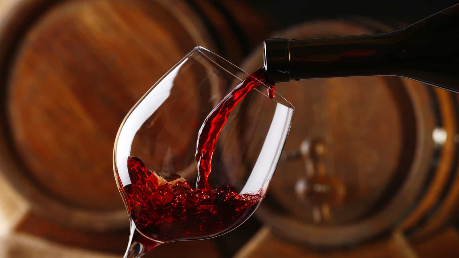 pouring red wine into a glass from a bottle on the background of barrels