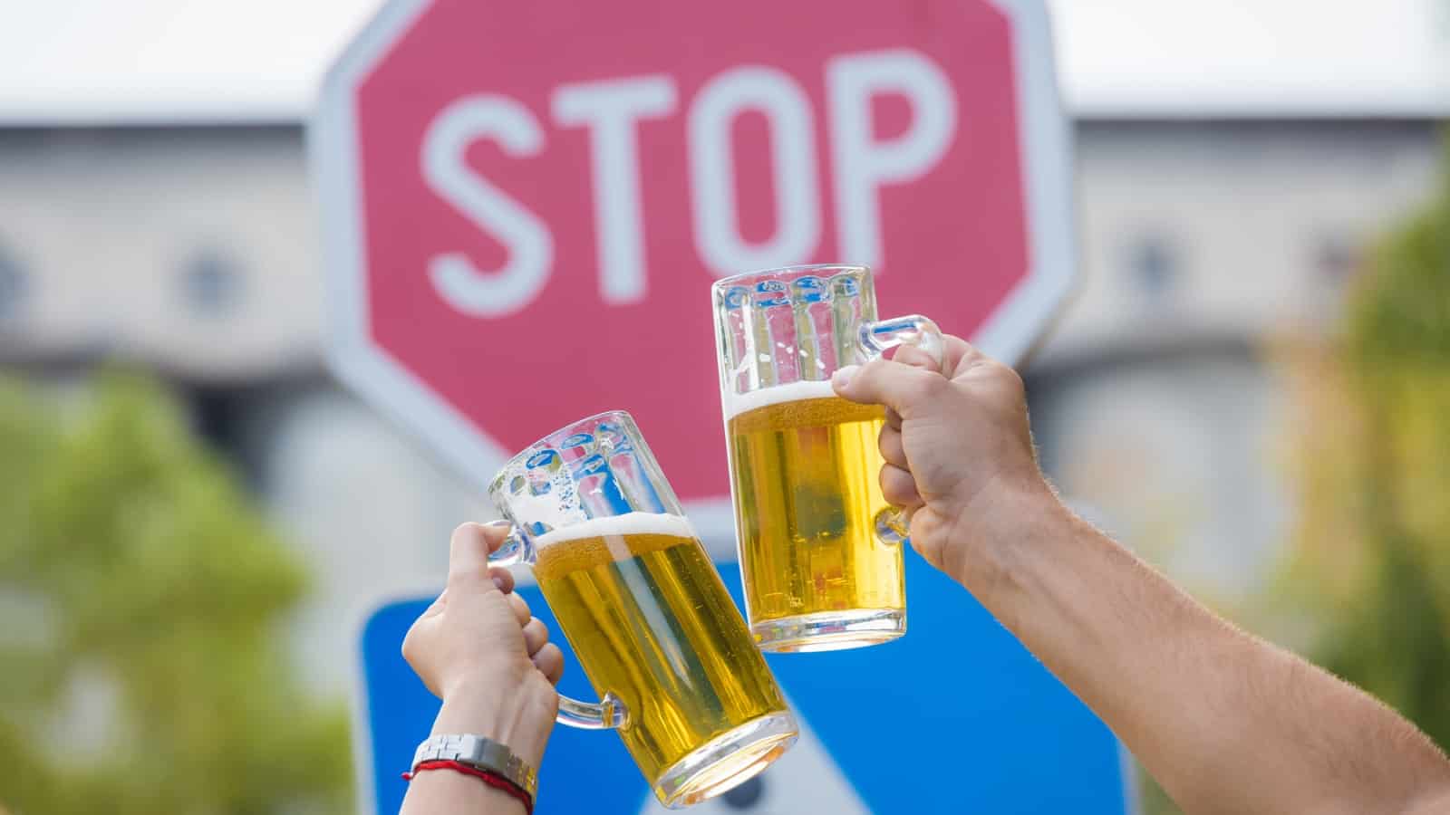 clinking glasses of beer in front of stop street sign