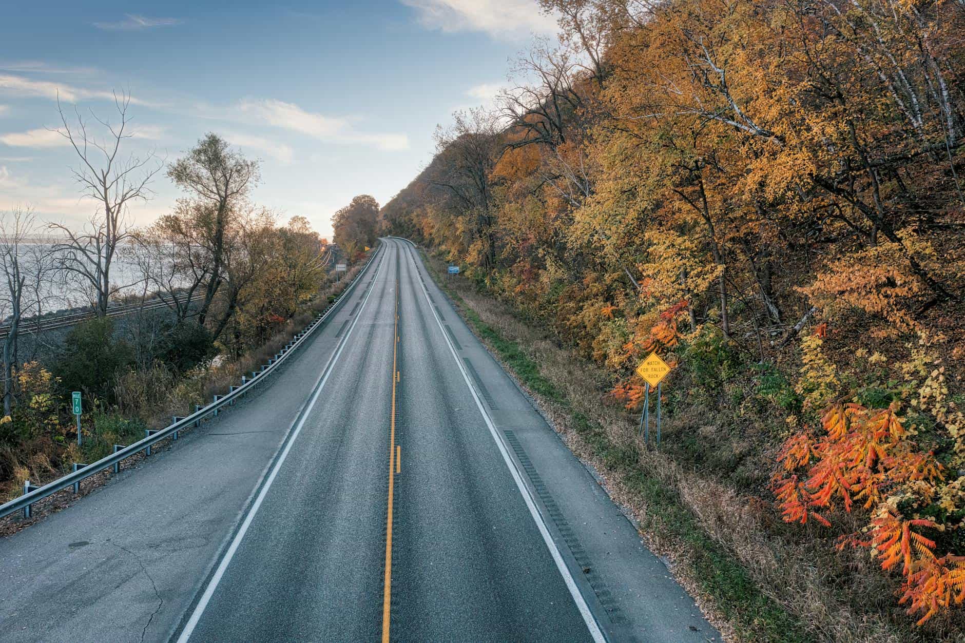 A picturesque autumn road flanked by colorful trees near a calm water body in Minnesota.