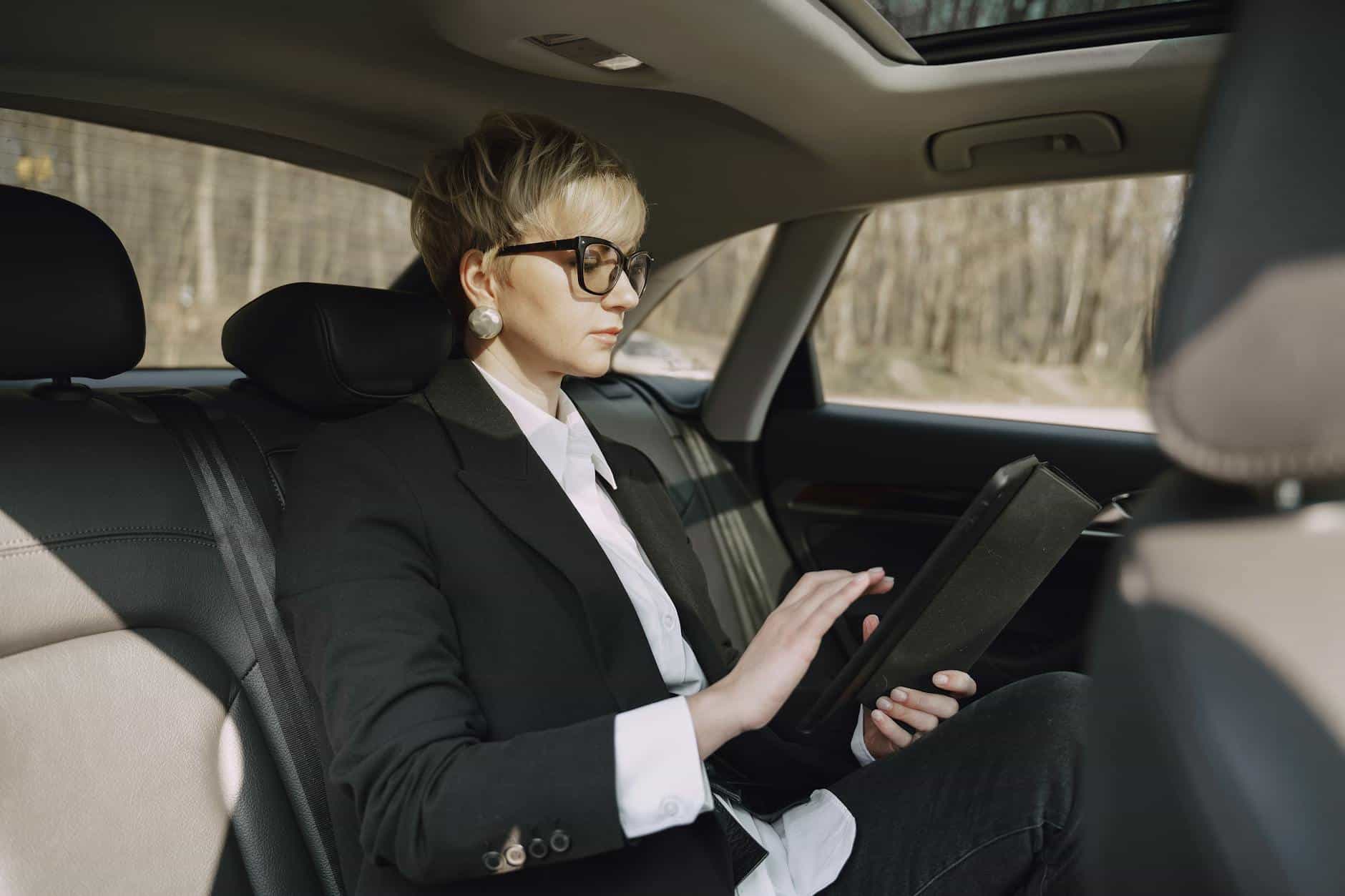 15 Road Trip Car Organizers for Traveling With Kids 3 Side view of focused female in stylish formal clothes using tablet while riding on backseat of modern car
