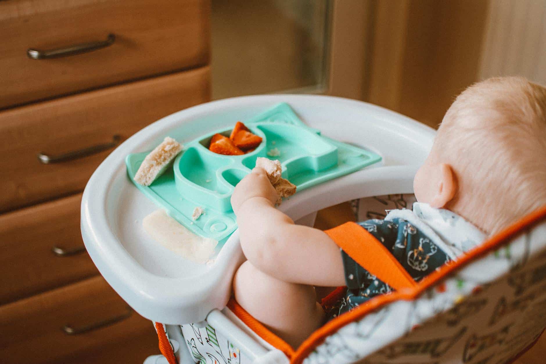 15 Road Trip Car Organizers for Traveling With Kids 12 A cute baby enjoying snack time in a high chair with colorful food tray indoors.