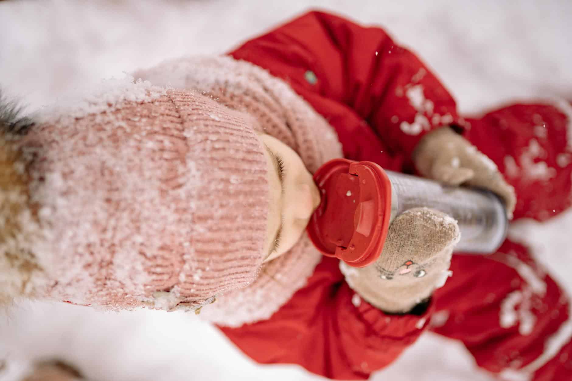 15 Road Trip Car Organizers for Traveling With Kids 13 A child in snow-proof clothes enjoys a drink from a tumbler in a snowy outdoor setting.
