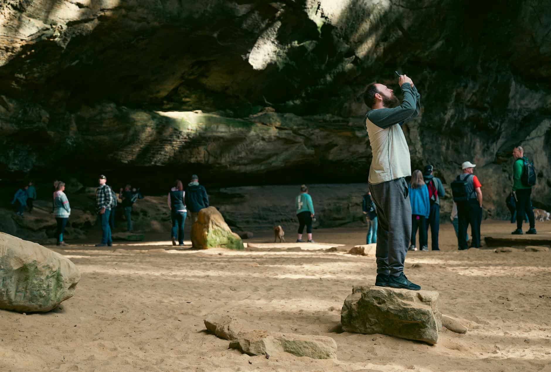 A tourist takes a photo inside a stunning cave with rock formations and visitors.