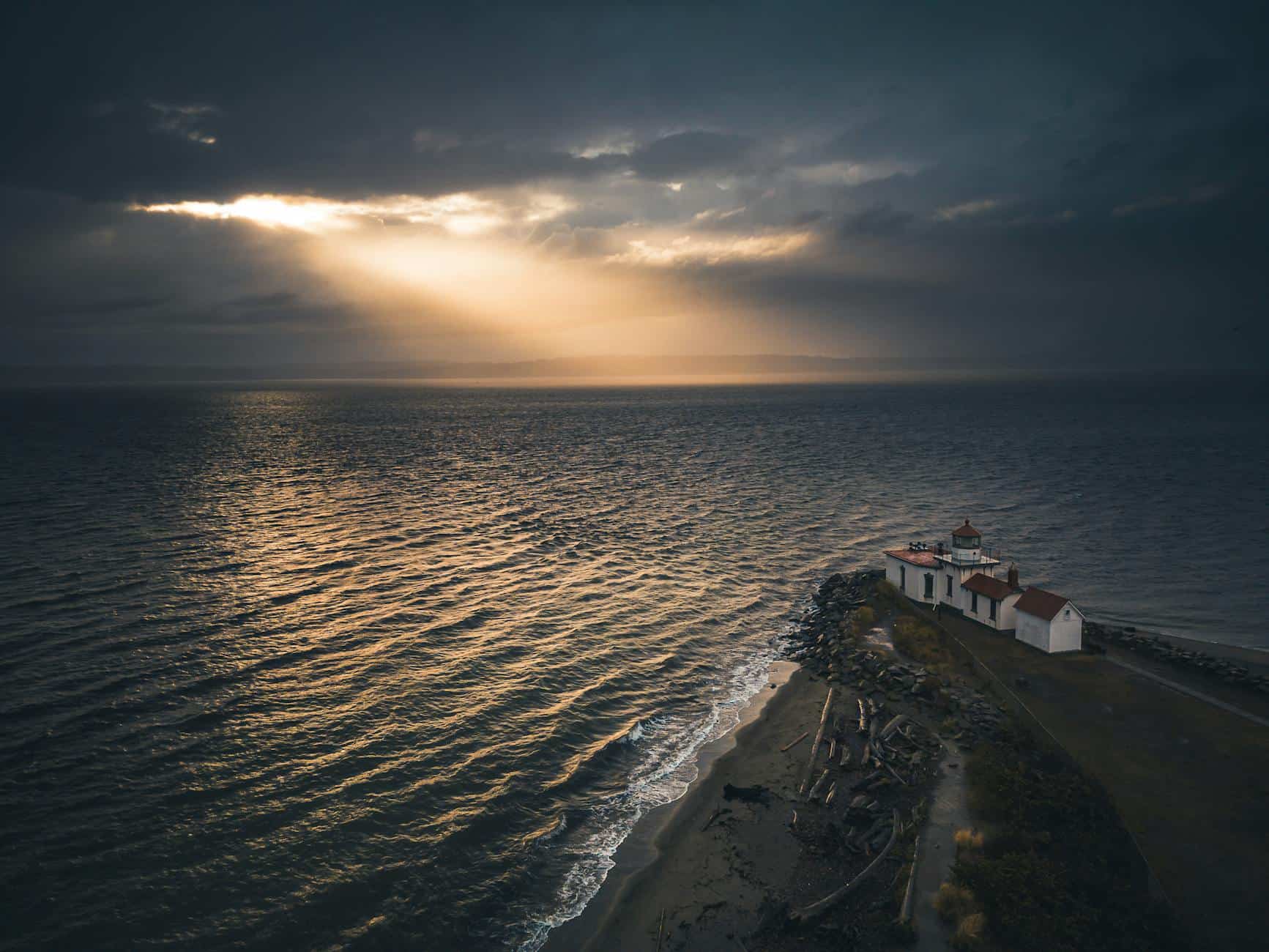 Stunning sunset view over West Point Lighthouse in Seattle with dramatic clouds and sun rays.