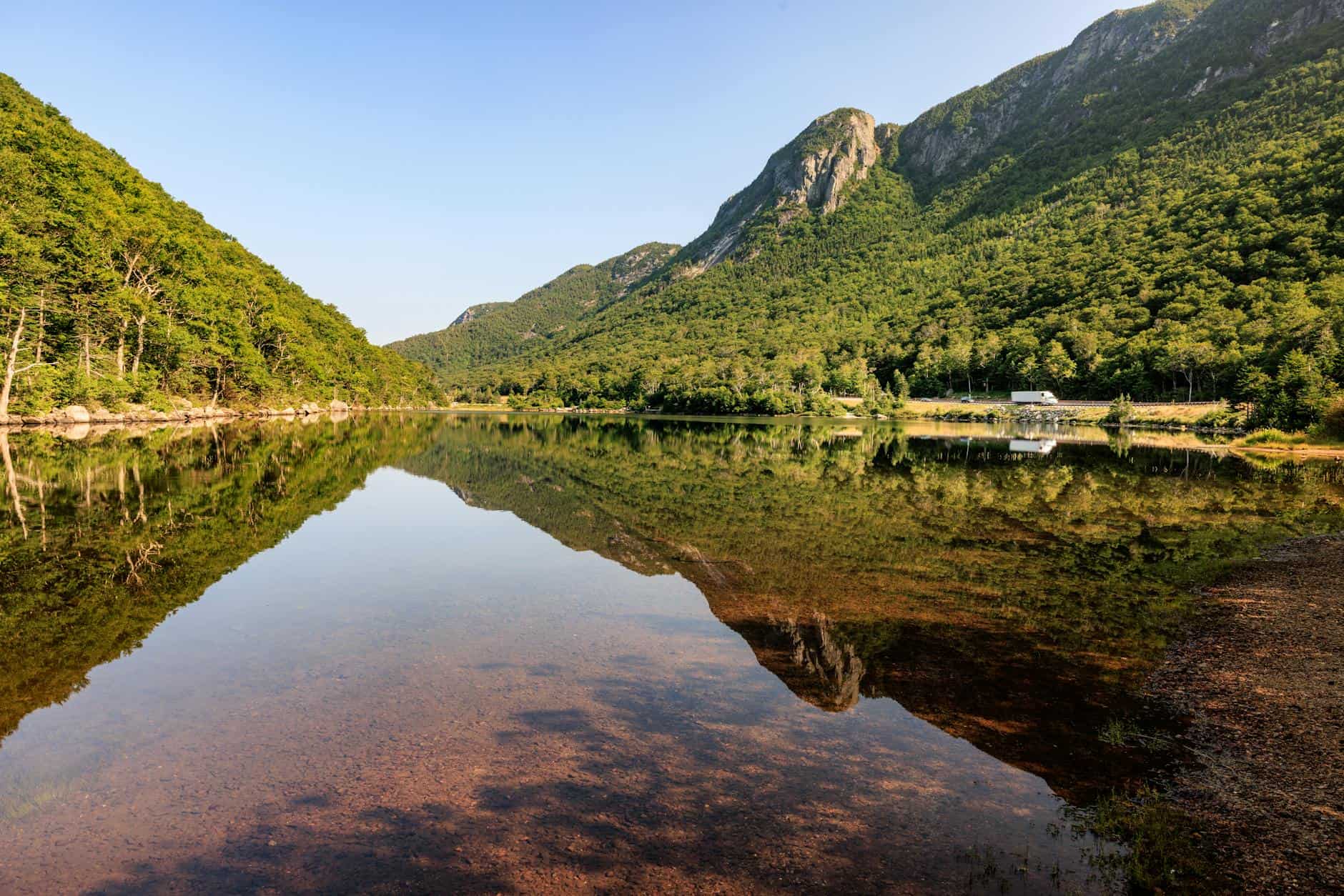 Captivating summer scene of a tranquil lake reflecting lush green mountains in Franconia Notch, New Hampshire.