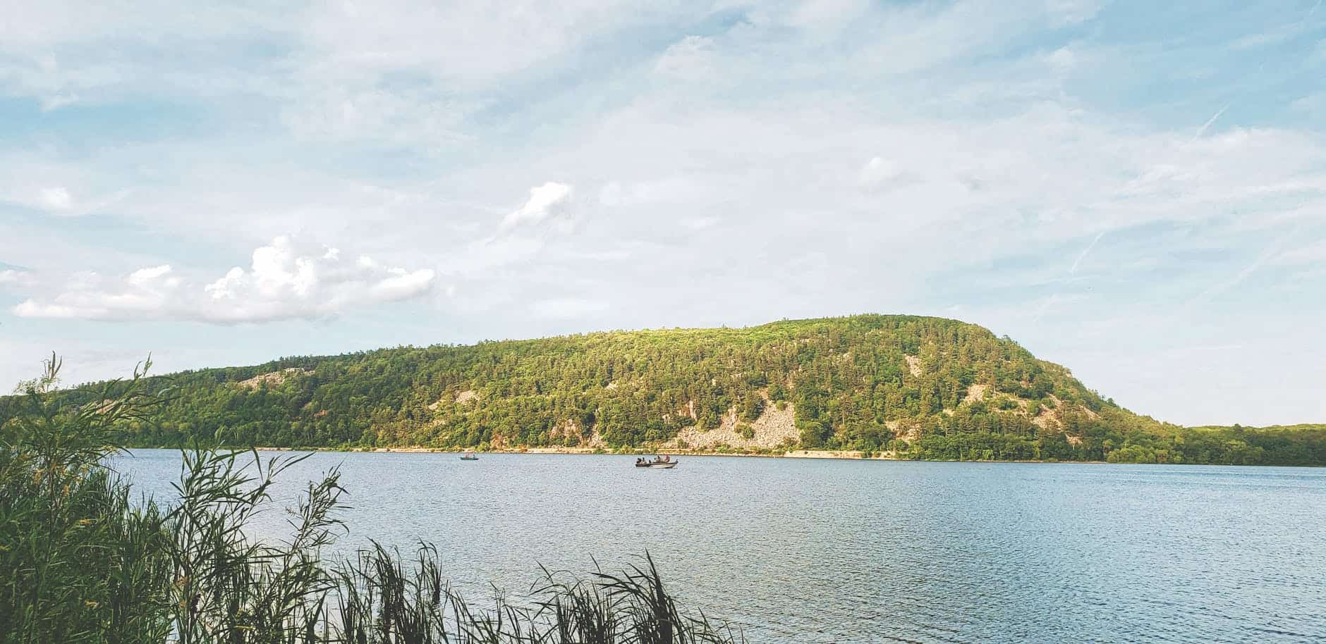 Peaceful landscape of a lake with boats and lush green hills on a sunny day in Wisconsin.
