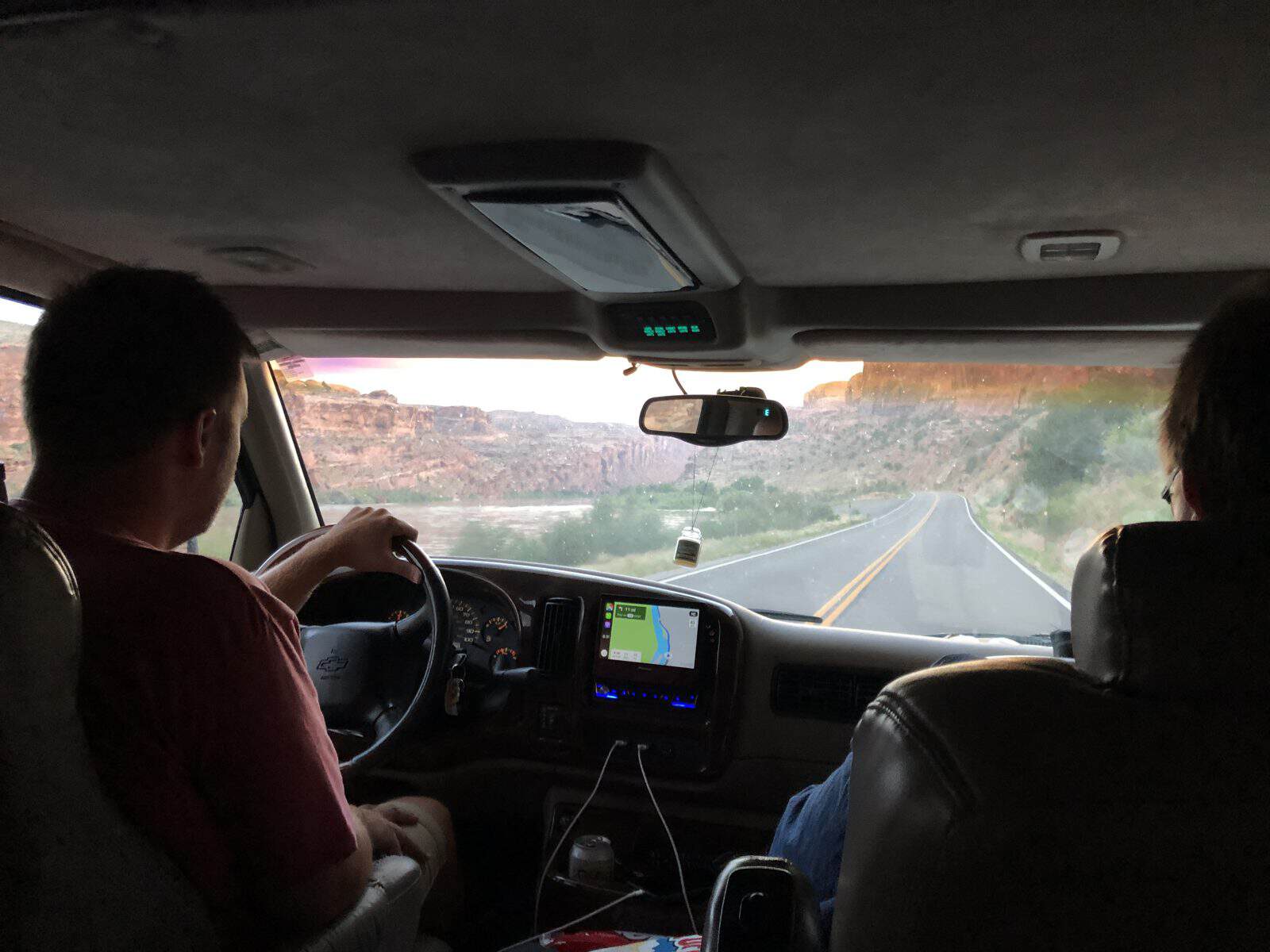 Two people in a car, view of road and canyon, navigation screen, interior details.