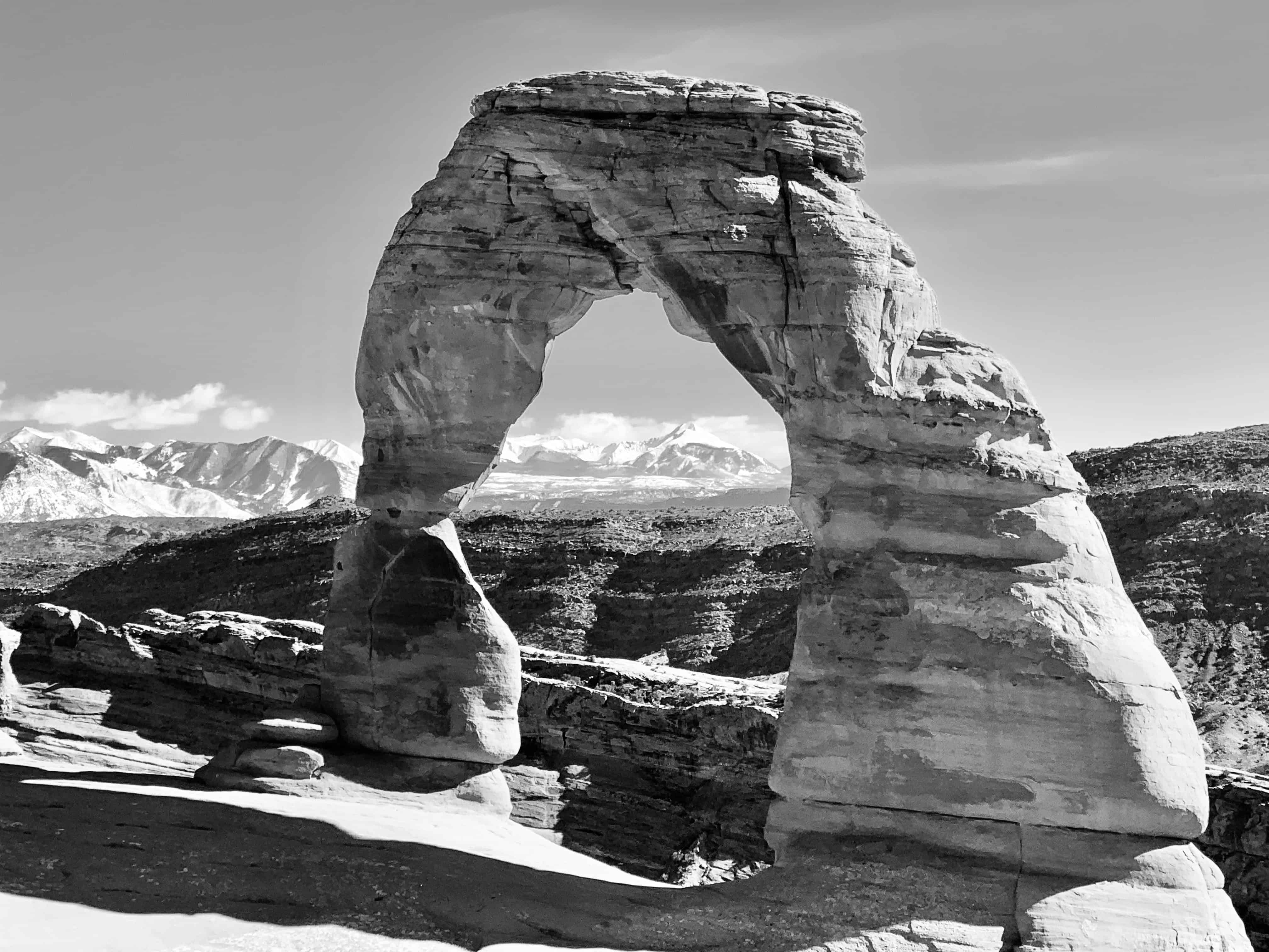 A rock arch framing distant mountains in black and white.