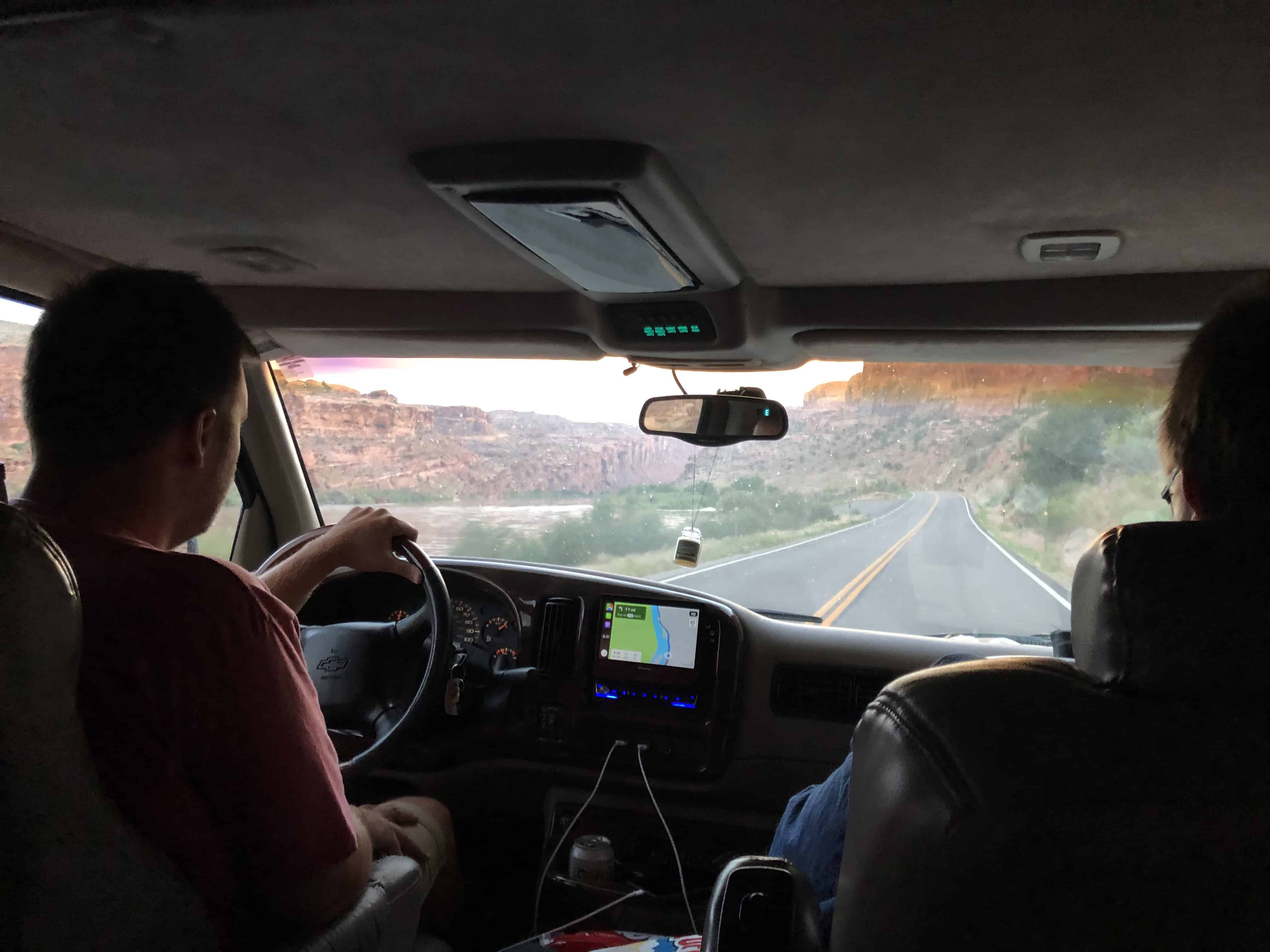 Two people in a car, view of road and canyon, navigation screen, interior details.