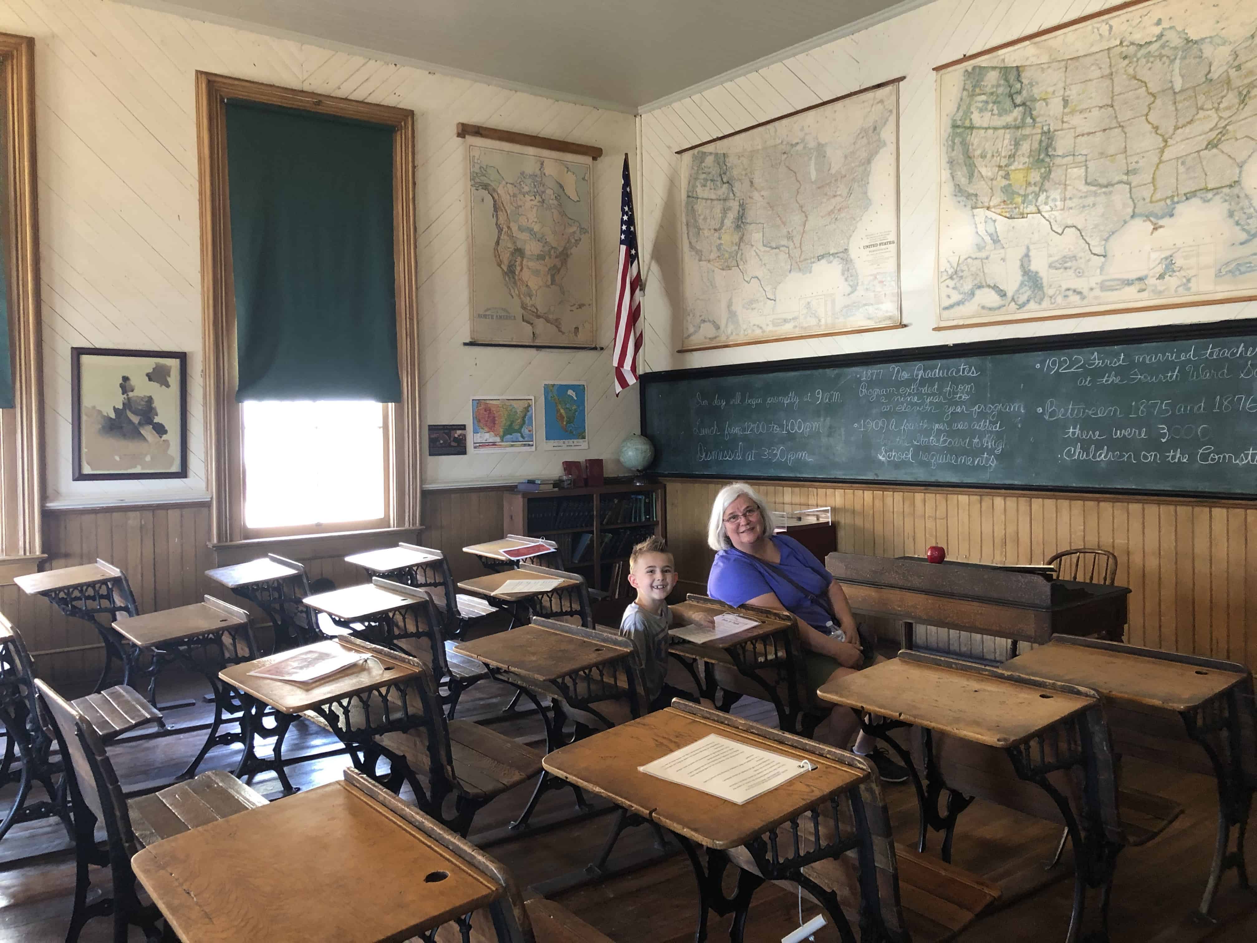 People photo in a vintage classroom with desks, maps, and a chalkboard.