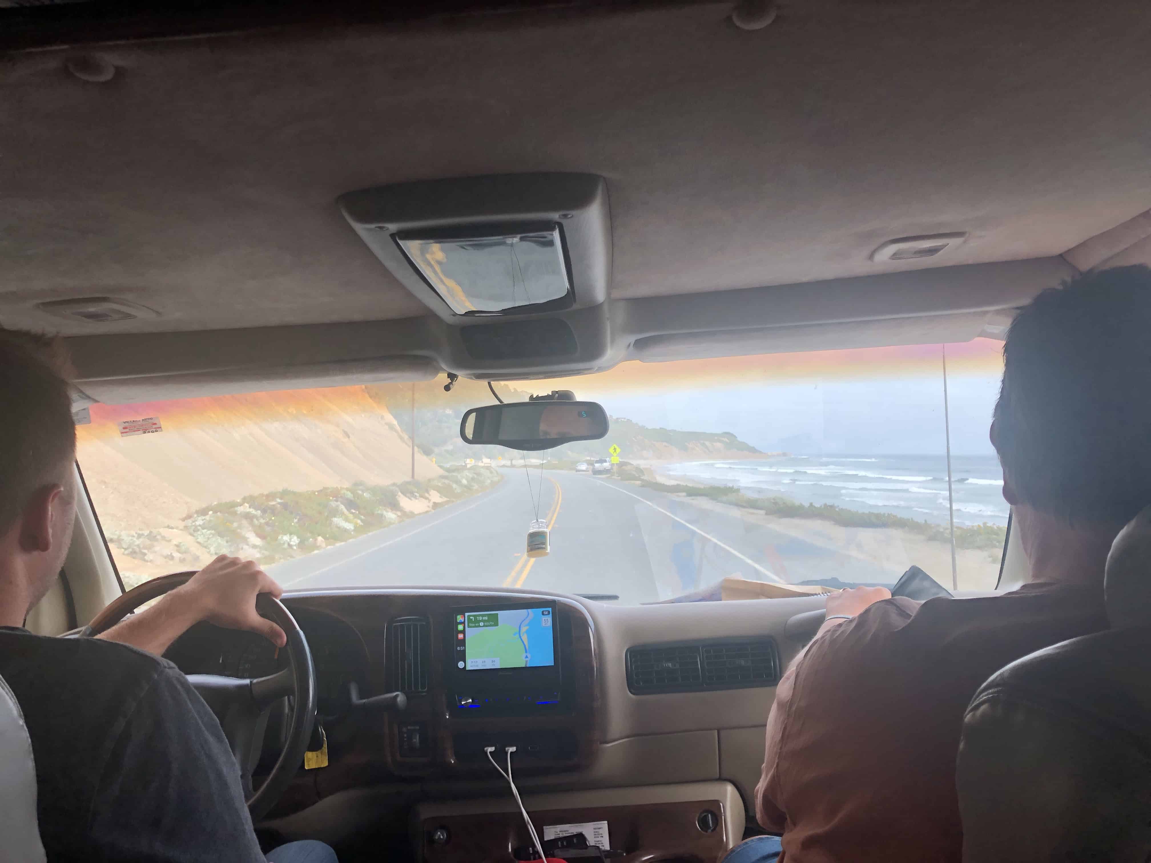 A coastal road and ocean seen through the front of the van.
