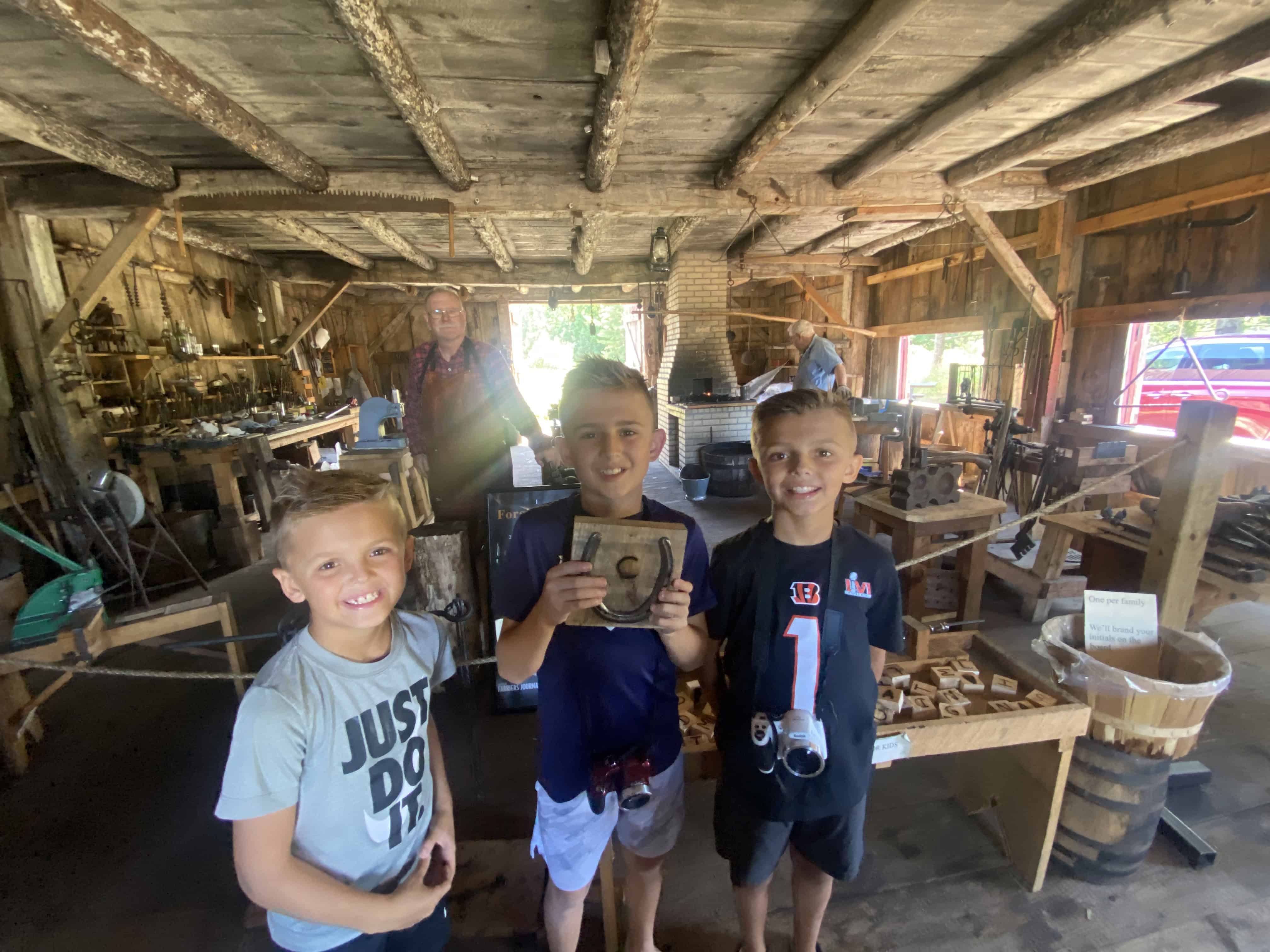 Three boys in a rustic wooden workshop, holding a wooden box, with a man in the background.