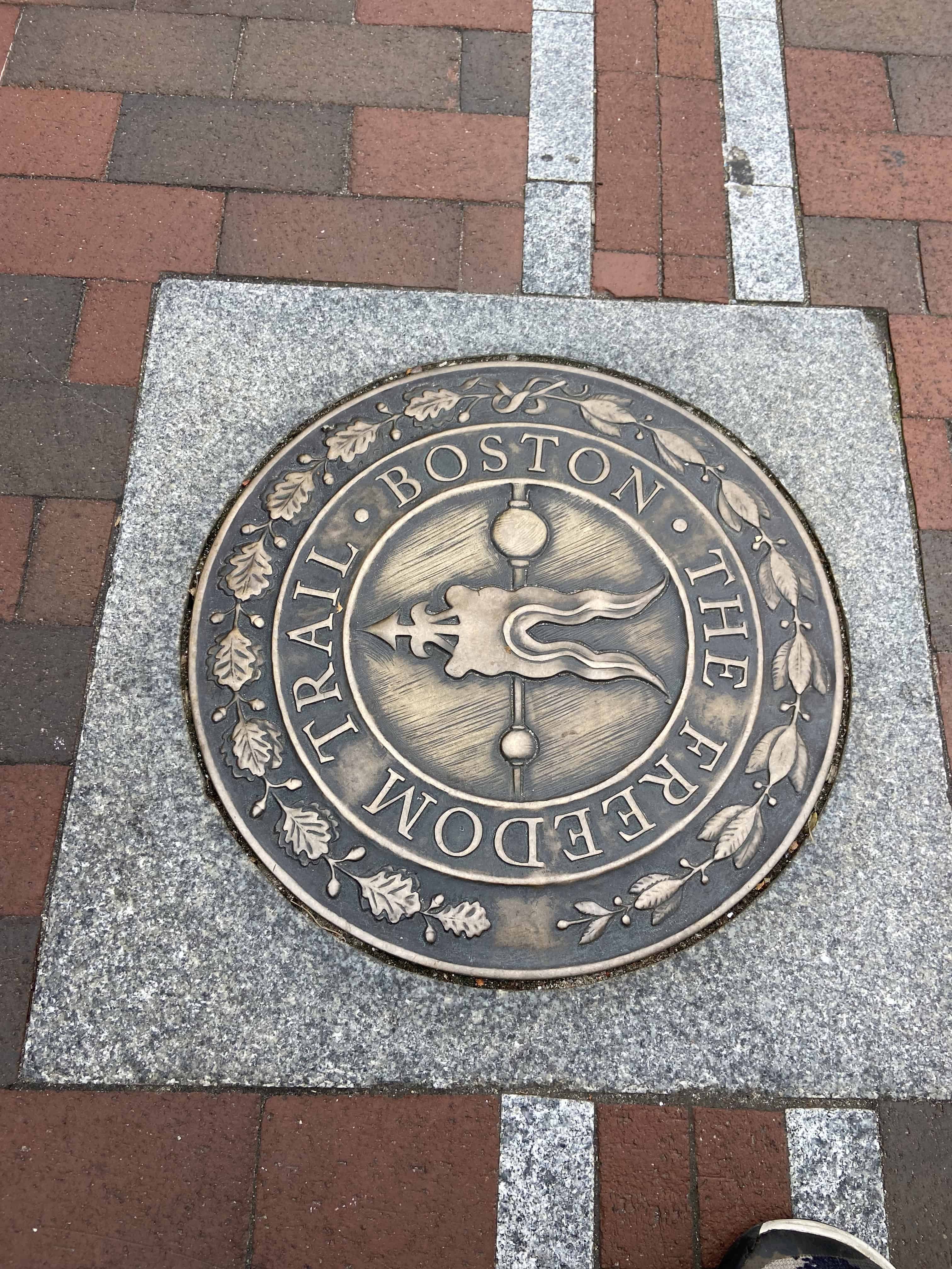 A bronze trail marker set into a brick walkway.